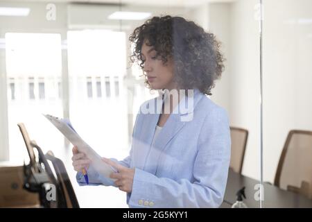 Young business woman with curly hair working in an office and doing paperwork. Stock Photo