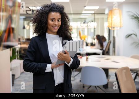 Young and happy african business woman holding paperwork smiling and looking at camera. Stock Photo