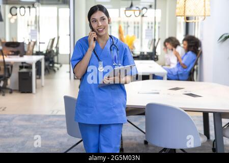 Young pretty nurse wearing blue uniform talking on the phone and looking at camera. Stock Photo