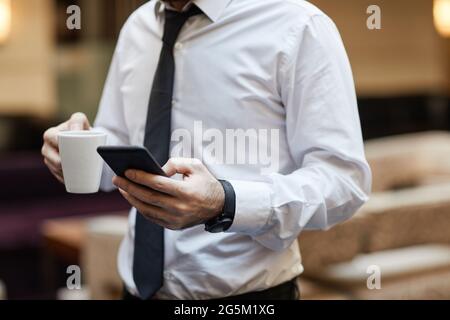 Cropped shot of unrecognizable businessman holding smartphone and coffee cup, copy space Stock Photo