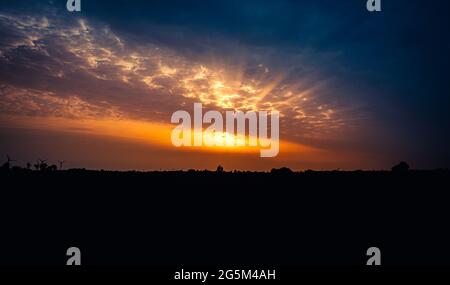 Dramatic sunbeams shining through blue clouds at sunset Stock Photo