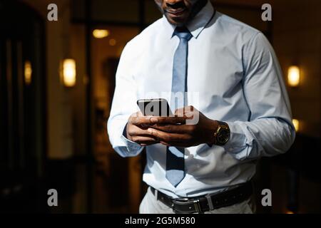 Cropped shot of unrecognizable African-American businessman using smartphone in sunlight, copy space Stock Photo