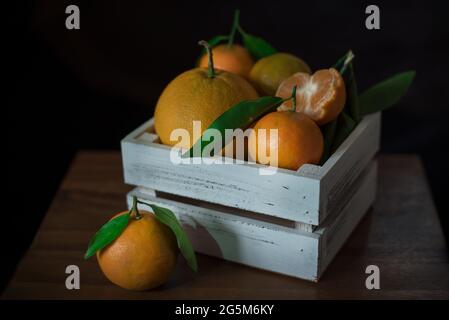 Fresh oranges and tangerines in a wooden box on a wooden table, close up, still life photography Stock Photo
