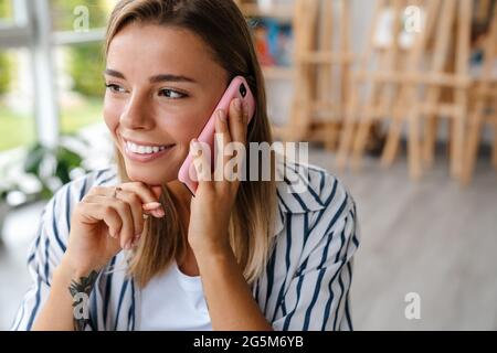 Smiling attractive young woman creative designer using mobile phone while working at the studio, close up Stock Photo