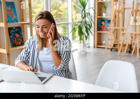 Smiling attractive young woman creative designer using mobile phone while working at the studio Stock Photo