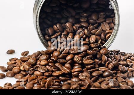 Open tin can and grains of black coffee on a white background. Fragrant roasted arabica beans on a white table. Traditional morning drink. Copy space. Stock Photo