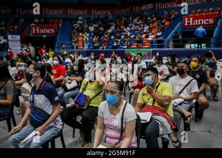 People wearing protective masks and face shields as precaution against the coronavirus disease queue as health workers inoculate patients with the COVID-19 Pfizer-BioNTech vaccine inside a sports stadium turned into a temporary vaccination site in San Juan City, Metro Manila, Philippines. Stock Photo
