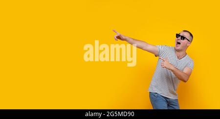 Portrait of funny young man in casual clothes pointing index fingers aside up isolated on yellow orange wall background in studio. People sincere Stock Photo
