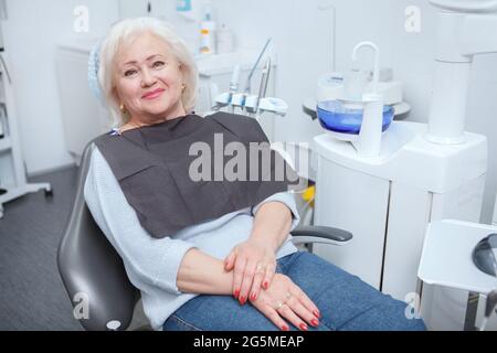 Charming senior woman smiling to the camera, sitting in dental chair at the clinic Stock Photo