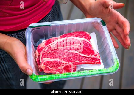 Red raw lamb meat shoulder chops from New Zealand packaged storebought with woman holding open plastic container showing Stock Photo