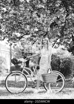 Amazing summer. travel. retro woman sell tulip flower bouquet. girl under sakura with vintage bicycle. spring beauty and fashion. cherry tree pink Stock Photo