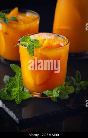 Summer cold drinks: homemade peach sangria with ice , and mint in glass on wooden black background Stock Photo