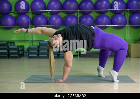 Fat woman is engaged in pilates in a fitness gym. A girl with a lot of  overweight trying to lose weight with the help of yoga, does exercises for  side Stock Photo 