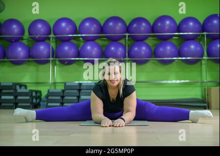 A fat woman is engaged in fitness in the gym. A girl with a lot of  overweight trying to lose weight with the help of sports, does stretching  exercises Stock Photo 