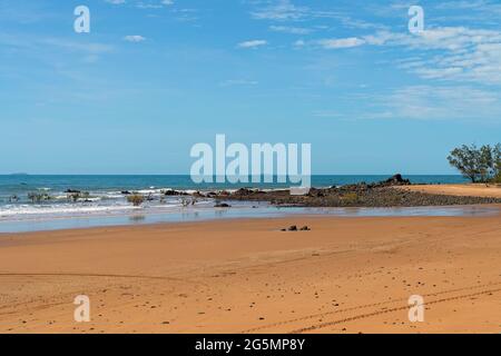 Waves towards exposed rocks on a sandy beach under a blue sky as the tide recedes Stock Photo