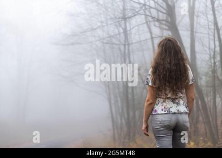 Back of young woman hiker on Cedar Cliffs forest woods trail in Wintergreen Resort, Virginia standing looking at view in morning fog foggy weather tre Stock Photo