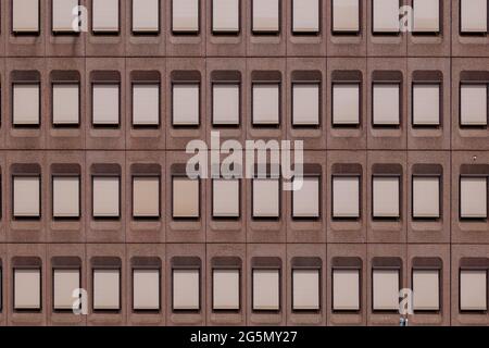 Outdoor exterior front view of modern earth tone pale red stone granite facade with typical rectangular windows with closed curtains Louvre. Stock Photo