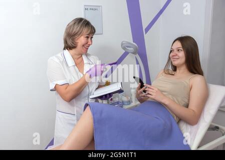 Professional cosmetologist. Female beauty doctor talking to her customer young woman while writing in the beauty clinic. Cosmetology concept