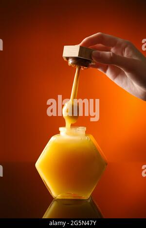 Woman pouring honey from dipper into glass jar on color background Stock Photo