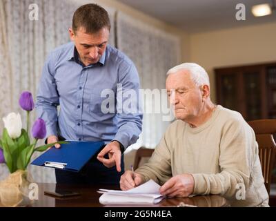 Elderly man and sales manager signing contract of purchase at home ...