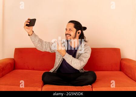 Young man using the smart phone taking a selfie at home in the living room Stock Photo