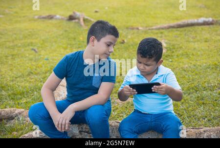 Latino brothers talking while looking at the cell phone sitting on the tree Stock Photo