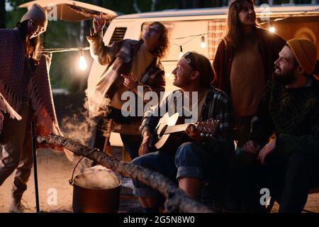 Happy young friends dancing and singing songs with guitar during camping in the forest Stock Photo