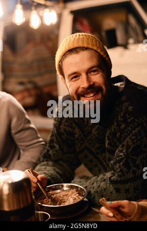 Young bearded man smiling at camera while having dinner on a picnic outdoors Stock Photo