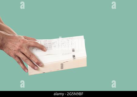 Hand holding and opening a thick book isolated on green pastel color background. Stock Photo