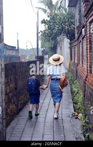 Mother and son holding hand walking on small pathway in Bali, Indonesia Stock Photo