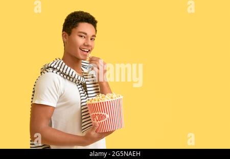 African-American teenager eating popcorn on color background Stock Photo