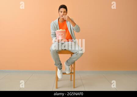 African-American teenager eating popcorn near color wall Stock Photo