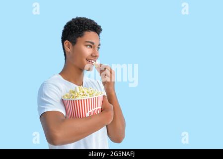 African-American teenager eating popcorn on color background Stock Photo