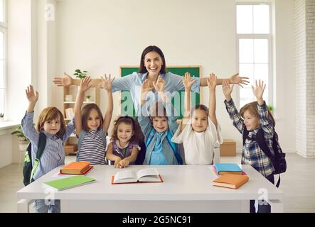 Happy teacher with arms widely spread to hug cheerful children raising hands Stock Photo