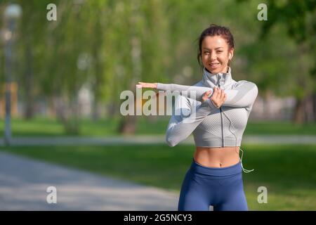 Portrait of a woman stretching shoulders for warming up before running or working out. Young female runner stretching arms before running at morning. Stock Photo