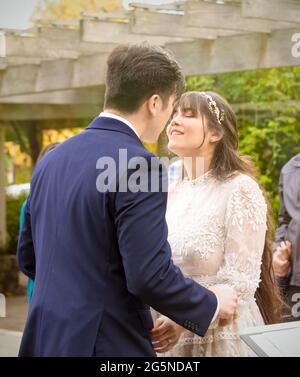 Biracial bride and groom preparing to kiss during wedding ceremony outdoors under pergola Stock Photo
