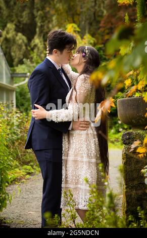 Biracial bride and groom outdoors kissing by stone wall in outdoor ceremony Stock Photo