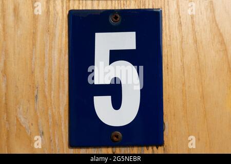 old blue enamel sign with white number 5 on a wooden wall Stock Photo