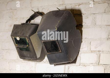 On a white wall hangs two welding masks Stock Photo