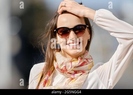 Closeup city portrait of smiling young woman in sunglasses in windy day Stock Photo