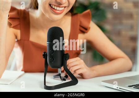 Closeup of young beautiful woman smiling sitting on desk using laptop and mic recording podcast while taking interview Stock Photo
