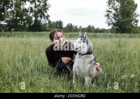 Owner girl playing with her siberian husky at field. Happy smiling woman with dog have a good time on weekend activity outdoors Stock Photo