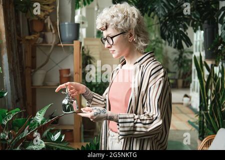 Young woman in eyeglasses caring about plants and waterig them in the garden Stock Photo