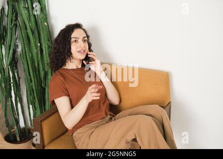 Young woman relaxing on the armchair and talking on mobile phone with her friend in the room Stock Photo