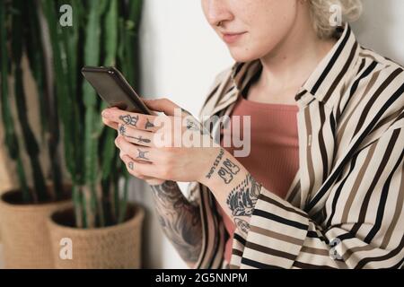 Close-up of young woman with tattoos on her hands holding mobile phone and working online Stock Photo