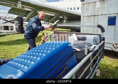 Security officer and detection dog checking luggage at aerodrome Stock Photo