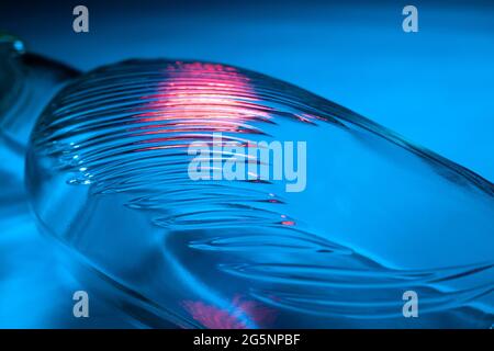 Abstract glass bottle background. Texture of wavy glass illuminated with multi-colored light. Pink and blue stains. Close up. Flares on glass Stock Photo