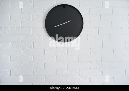 Minimalistic black clock on a white brick wall in the interior Stock Photo