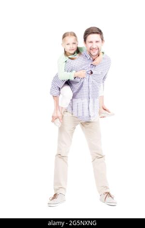 Vertical full length isolated shot of joyful mature man with beard on face having fun with his little daughter carrying her on back, white background Stock Photo