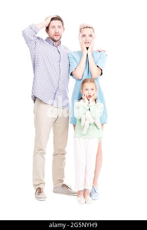 Vertical full length shot of modern man and woman standing with their little daughter astonished at something, white background Stock Photo